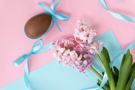 Easter background with chocolate egg with blue bow and pink hyacinth flowers, with blue ribbon on...