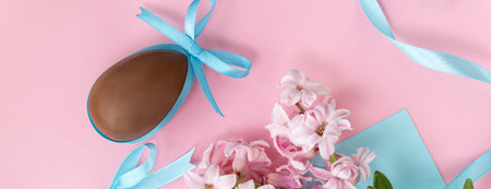banner with Easter background with chocolate egg with blue bow and pink hyacinth flowers, with blue ribbon on pastel pink and blue colors. Happy Easter concept.の写真素材