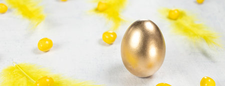 banner with golden egg on a white concrete background with yellow feathers and yellow chocolates in...