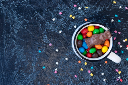 chocolate bunny on multi-colored chocolates in the form of eggs in a white mug on a black...