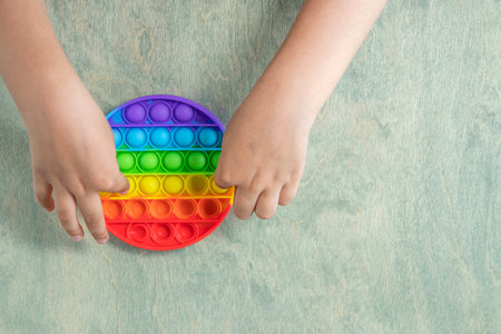 boy pressing on colorful rainbow squishy soft silicone bubbles. Kid playing with pop it sensory toy. Stress and anxiety relief. Trendy fidgeting game. top viewの写真素材
