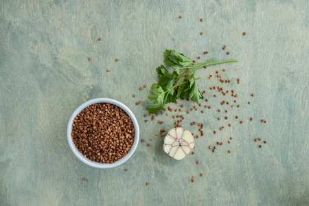 top view on buckwheat with spices on a green wooden background. buckwheat in white plate with garlic and parsley. Copy space. Top viewの写真素材