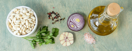 banner with top view on wite beans in white plate with onion, parsley pepper, and pink salt. recipe, food composition, nutrition concept. wite beans with spices and olive oil on wooden background. Copy spaceの写真素材