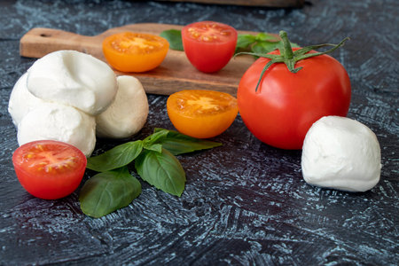 mozzarella balls, tomatoes, and basil on black background. Ingredients of Italian caprese salad....