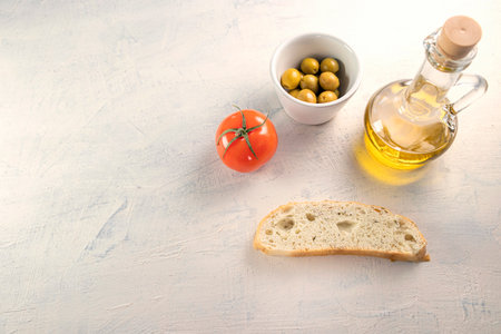 a slice of bread with olives, tomato and olive oil on white textured background. top view. flat lay. soft focusの写真素材