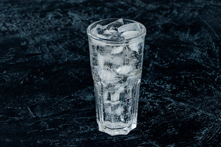 A glass with ice water and ice cubes on a black textured background. A refreshing and chilling drink in hot weather. Isolate with copy space.の写真素材