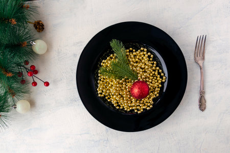 flat lay Christmas decorations, golden beads, branches of a Christmas tree and a red Christmas ball in a black plate, like Italian pasta. festive food concept for christmas or new year. top viewの写真素材