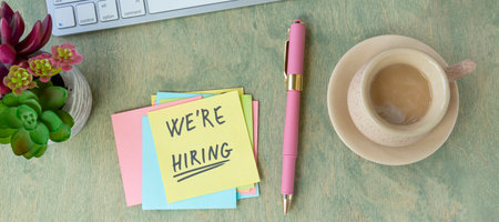 banner with flat lay on desktop with notes with the words you are taken We're Hiring, keyboard, pen, cactus, mouse and a cup of coffee. top viewの写真素材