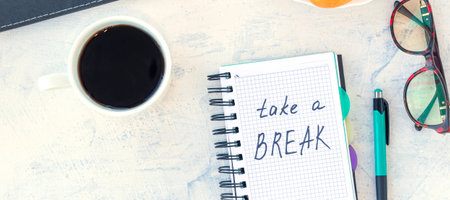 banner with words Take a break. Concept time off. Words Take a break in a notebook on the working table with cup of coffee and bun. Top view.の写真素材