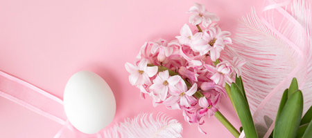banner with Easter background with white egg and pink hyacinth flowers, with pink ribbon and white feathers on pastel pink colors. Happy Easter concept. top viewの写真素材