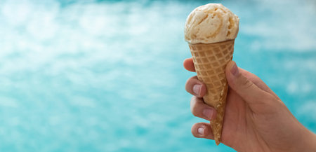 banner with young hand holds an ice cream cone on the background of the blue water of the sea. the...