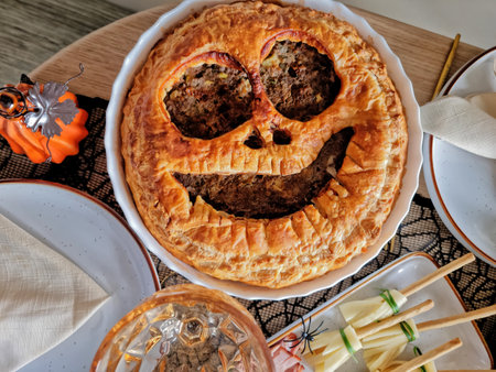table setting for a Halloween party. Appetizing, rosy, baked meat pie in the shape of Jack OLantern....