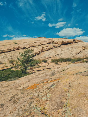 Vertical photo of the volcanic mountains of Bektau Ata with scattered green bushes in the foreground and a blue sky with small clouds above.の写真素材