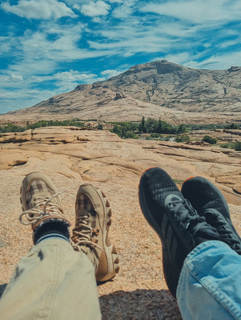 Vertical soft-focus photo showing a man s and woman s legs in sneakers standing with volcanic mountains blurred in the background.の写真素材