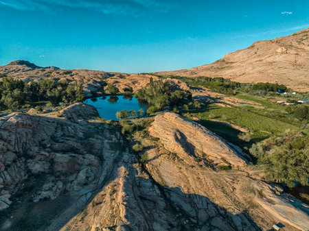 Aerial top view of a vibrant blue lake bordered by green vegetation and volcanic mountains under clear sky on a sunny day.の写真素材