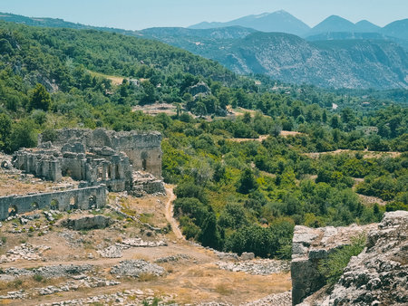 View of the ancient city ruins of Tlos in Turkey, surrounded by lush green forests and distant mountains under clear skies.の写真素材