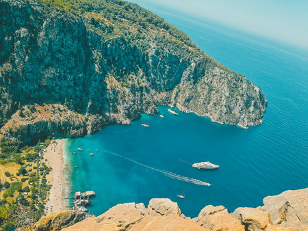 Top view of a sandy beach nestled between rocky cliffs in a sea bay, with yachts and boats floating on turquoise water in Turkey.の写真素材