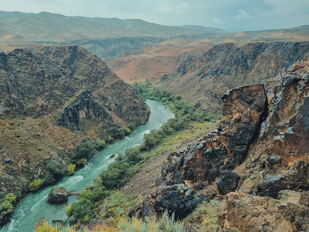 A fast-flowing mountain river rushes between steep black rock walls in the canyon, under a cloudy sky.の写真素材