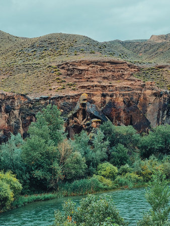 Vertical photo of a river flowing near black rocky formations with rolling hills in the background...