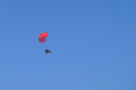 Two men flying in motor paraplan with red wing on blue sky background.の写真素材