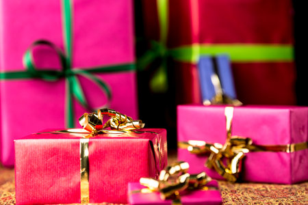 Six gift boxes wrapped in magenta, crimson and blue  Focus is on the golden bow around the small crimson box in the front  Ready as background for any gift-giving occasion の写真素材