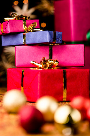 Four Christmas gift boxes with golden bows piled up  Tight framing, vibrant colors  Blurred baubles in the foreground  Background for Xmas gift-giving の写真素材