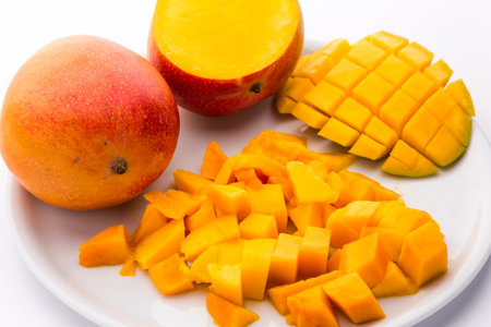 Many juicy mango pulp cubes. A third of a mango cut in a rectangular pattern to shape dice that remain attached to the peel. A mango cut open in cross section and an entire fruit. White background.の写真素材