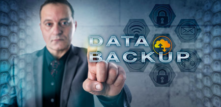 Male information manager is activating DATA BACKUP onscreen. Data clusters are mirrored on each side of the frame. Data security concept and metaphor for business continuity and disaster recovery.の写真素材