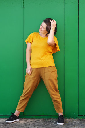 Beautiful young brunette woman wearing yellow blouse looking aside of camera. Green colored metal texture background.  Vertical image with space for text and desing.の写真素材