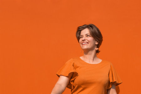 Attractive young smiling woman having fun in beautiful sunny day. Outdoor portrait of pretty brunette female model looking away of camera. Metal texture orange color wall on background. Head shot.の写真素材