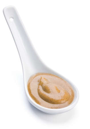 Mustard yellow sauce in ceramic spoon on whiteの写真素材