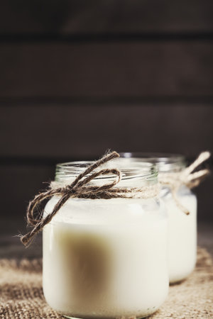 Fresh cow milk or cream in glass bottles, rustic style, vintage wood backgroundの写真素材
