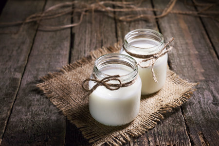 Fresh cow milk or cream in glass bottles, rustic style, vintage wood backgroundの写真素材