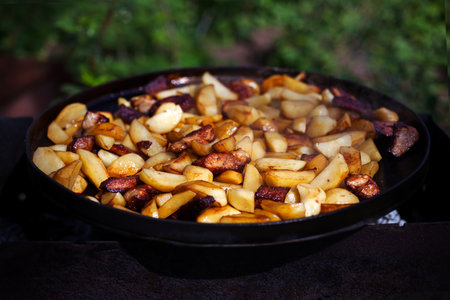 Beef meat stewed with potatoes on barbecue. Slice potatoes are prepared on the grill on sunny day. Close up. Culinary concept.の写真素材