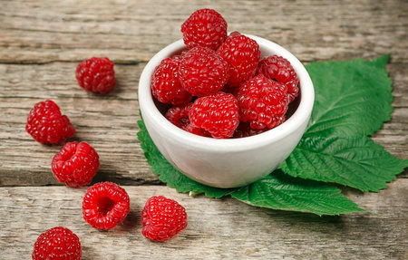 Red fresh raspberries on white rustic wood background. Bowl with natural ripe organic berries with...