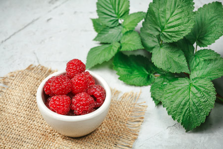 Red fresh raspberries on white rustic wood background. Bowl with natural ripe organic berries with...