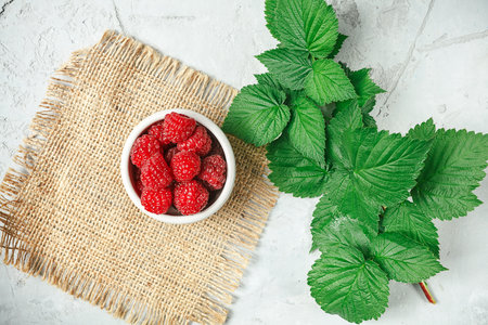Red fresh raspberries on white rustic wood background. Bowl with natural ripe organic berries with...