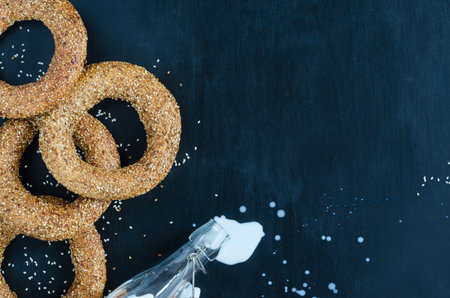 Turkish simit bagel dusted with sesame and spilled milk from a bottle on a black background. Top view. Banner background with copy spaceの写真素材
