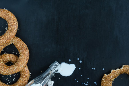 Turkish simit bagel dusted with sesame and spilled milk from a bottle on a black background. Top view. Banner background with copy spaceの写真素材