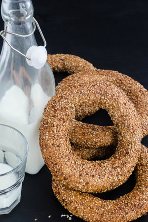 Turkish simit bagels with sesame, a bottle of milk and a glass on a wooden table. Black backgroundの写真素材