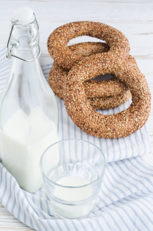 Turkish simit bagels with sesame, a bottle of milk and a glass on a wooden table. Cotton fabric and...