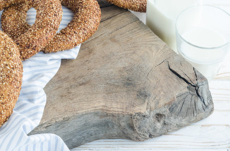 Turkish simit bagels with sesame on a wooden board. A bottle of milk, a glass, cotton cloth. Copy spaceの写真素材