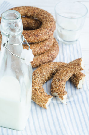 Turkish simit bagels with sesame, a bottle of milk and a glass on a wooden table. Cotton fabric and blur backgroundの写真素材