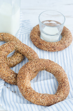 Turkish simit bagels with sesame, a bottle of milk and a glass on a wooden table. Cotton fabric and blur backgroundの写真素材