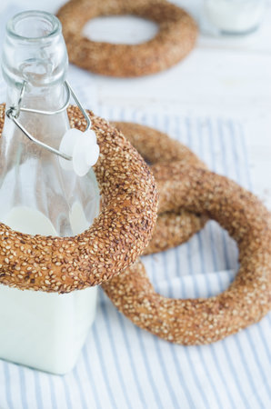 Turkish simit bagels with sesame, a bottle of milk and a glass on a wooden table. Cotton fabric and...