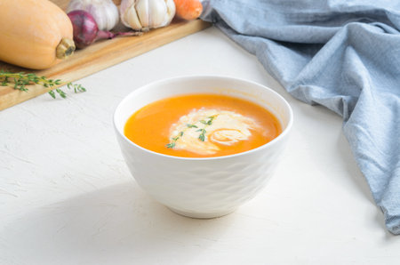 Pumpkin cream soup on a white table. Board Shallot Thyme Carrot Garlic Napkin Broccoli Pumpkin. Copy spaceの写真素材
