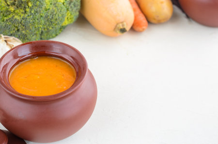 Pumpkin cream soup in a ceramic bowl on a white table. Garlic Carrot Broccoli Pumpkin. Copy spaceの写真素材