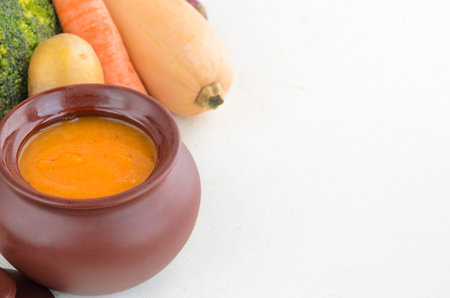Pumpkin cream soup in a ceramic bowl on a white table. Garlic Carrot Broccoli Pumpkin. Copy spaceの写真素材