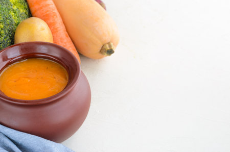 Pumpkin cream soup in a ceramic bowl on a white table. Napkin Garlic Carrot Broccoli Pumpkin. Copy spaceの写真素材