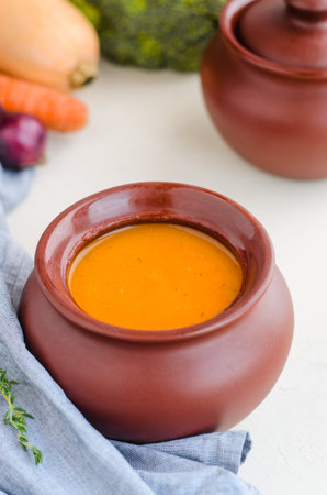 Pumpkin cream soup in a ceramic bowl on a white table. Napkin Thyme Garlic Carrot Broccoli Pumpkin. Copy spaceの写真素材